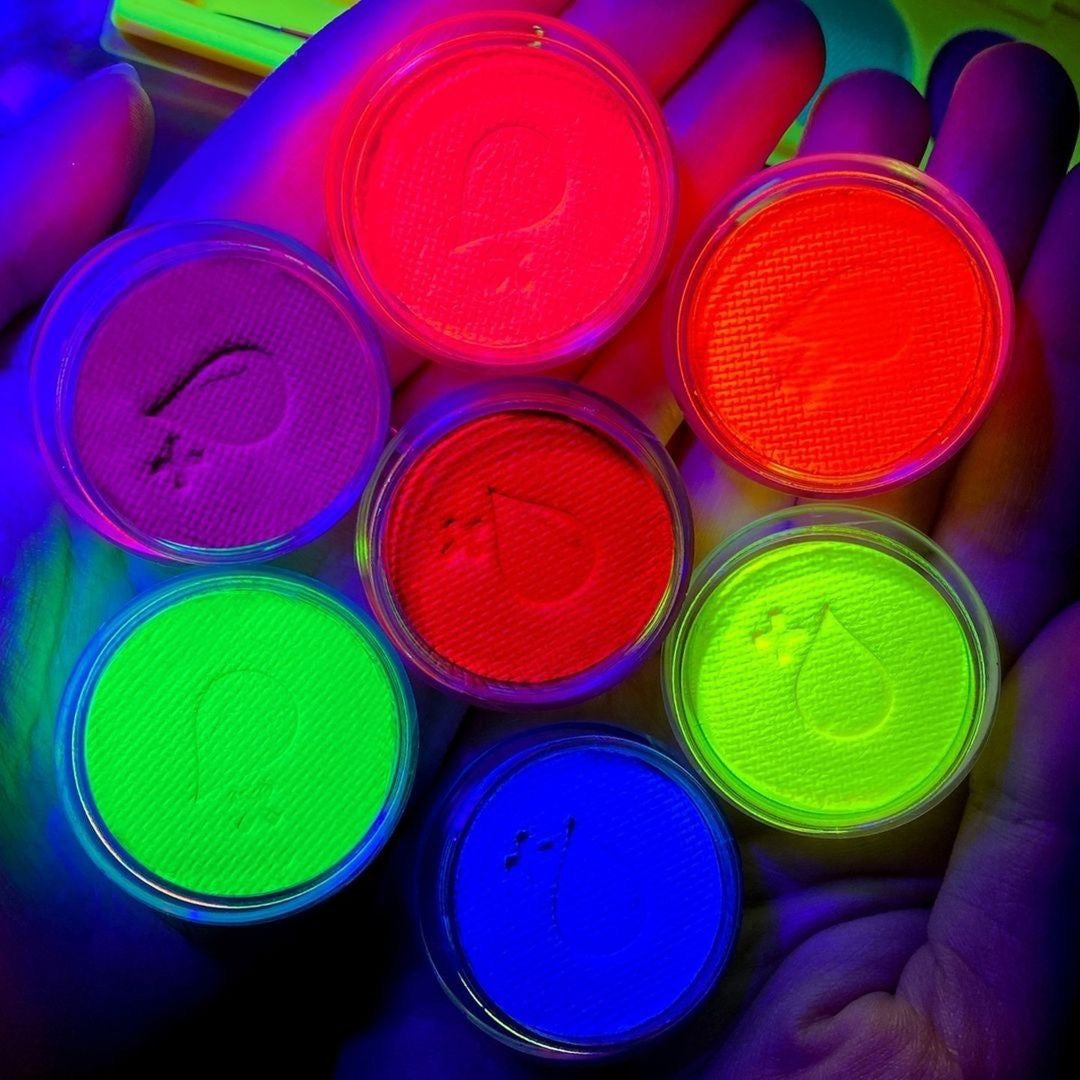 Hot pink, blue, and green eyeliner cakes glowing under blacklight